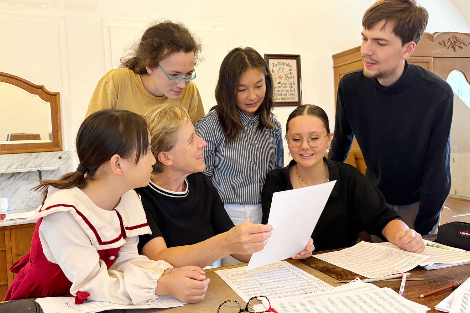 Fünf Jugendliche sitzen und stehen am Tisch um die Komponistin Annette Schlünz herum, die ein Notenblatt in ihrer Hand hält