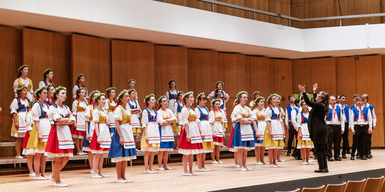 Eine Dirigentin bei der Arbeit mit ihrem Chor in tschechischen Trachten