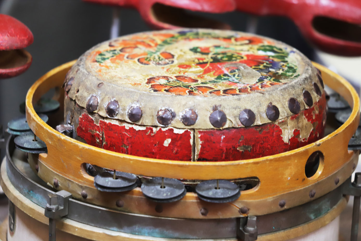 In einem hölzernen Schellenkranz steht eine sehr kleine, bunt bemalte Trommel. Sie ist ihrem relativ verwitterten Aussehen nach zu urteilen schon alt, die Farbe blättert an mehreren Stellen ab. Das Fell der Trommel wird von Metallnieten gehalten.
