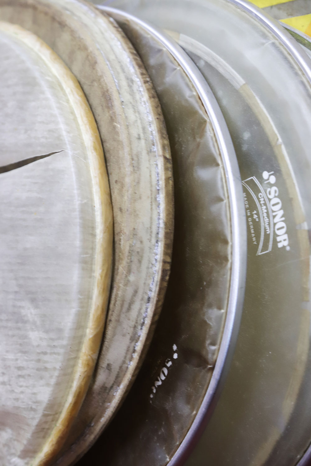 Mehrere Trommelfelle verschiedener Größen und Materialien sind übereinandergeschichtet. Die dünnen Metallriemen, an denen sie befestigt sind, sind zu erkennen.