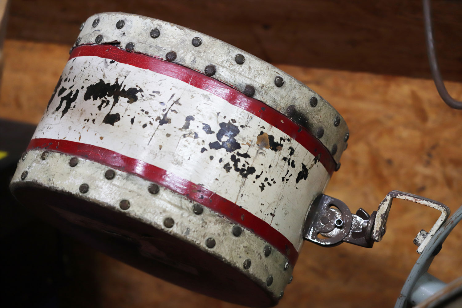 Eine dem Anschein nach recht kleine, weiße Trommel mit zwei roten Streifen ist an einer neigungsverstellbaren Halterung befestigt. Oben und unten ist sie ringsherum mit Nägeln beschlagen, in der Mitte blättert die weiße Farbe schon etwas ab.)