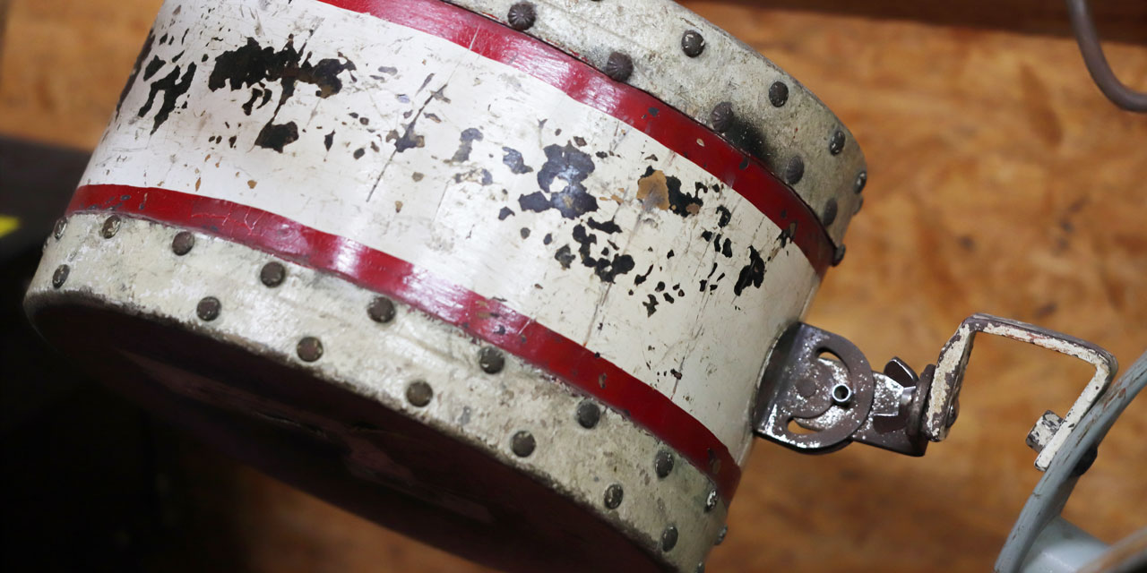 Eine dem Anschein nach recht kleine, weiße Trommel mit zwei roten Streifen ist an einer neigungsverstellbaren Halterung befestigt. Oben und unten ist sie ringsherum mit Nägeln beschlagen, in der Mitte blättert die weiße Farbe schon etwas ab.