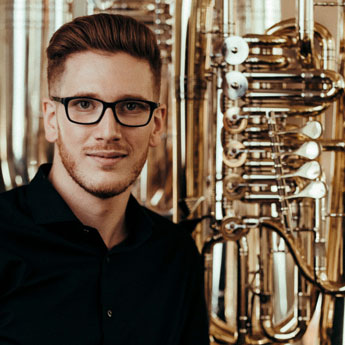 Constantin Hartwig, braune Haare und (Stoppel) Bart, schwarzes Hemd, schwarze Brille 