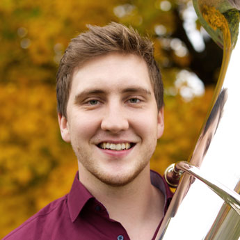 Donath Rehm, blonde Haare, rotes Hemd, lächelt in die Kamera, scheint Tuba neben sich zu halten