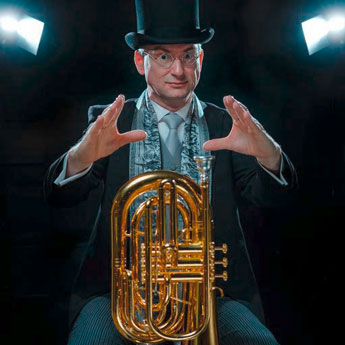 KV Prof. Jörg Wachsmuth, schwarzer Anzug, Zylinder, Brille, umgekehrte Tuba zwischen Beine geklemmt