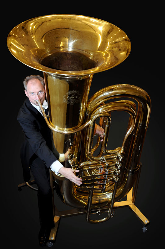 Prof. Jörg Wachsmuth spielt die Riesentuba Ilse, diese steht auf einem Gestell mit Rollen und ist deutlich größer als er selbst 