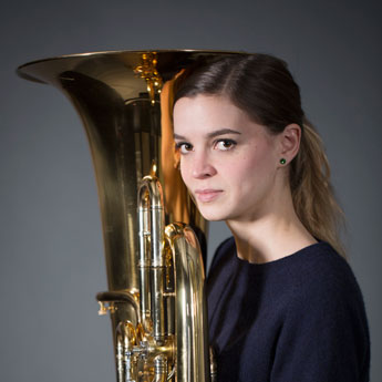 Ruth Ellendorff, braunblonde Haare als Pferdeschwanz, dunkelblauen Oberteil und dunkelblauer Ohrring, schaut seitlich in die Kamera, mit Tuba direkt vor dem Körper 