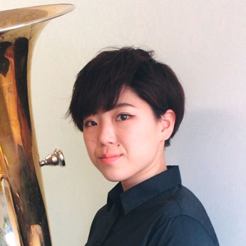 Shiho Murano, kurze, dunkelbraune bis schwarze Haare, schwarzes Hemd, hält Tuba vor sich und blickt leicht lächelnd seitlich in Kamera	