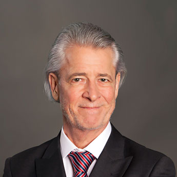 Walter Hilgers, mittellange grauweiße, zurückgegelte Haare, schwarzes Jackett, weißes Hemd, bunte Krawatte, lächelt leicht in Kamera