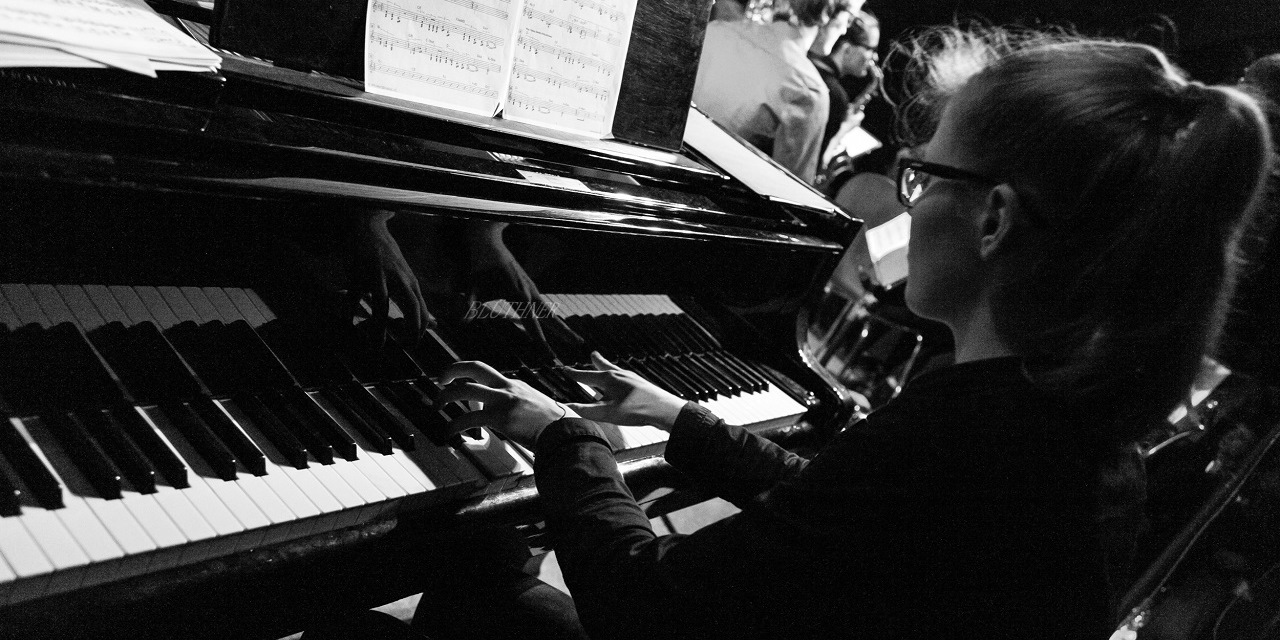 Eine Pianistin mit Zopf und Brille spielt ihr Instrument