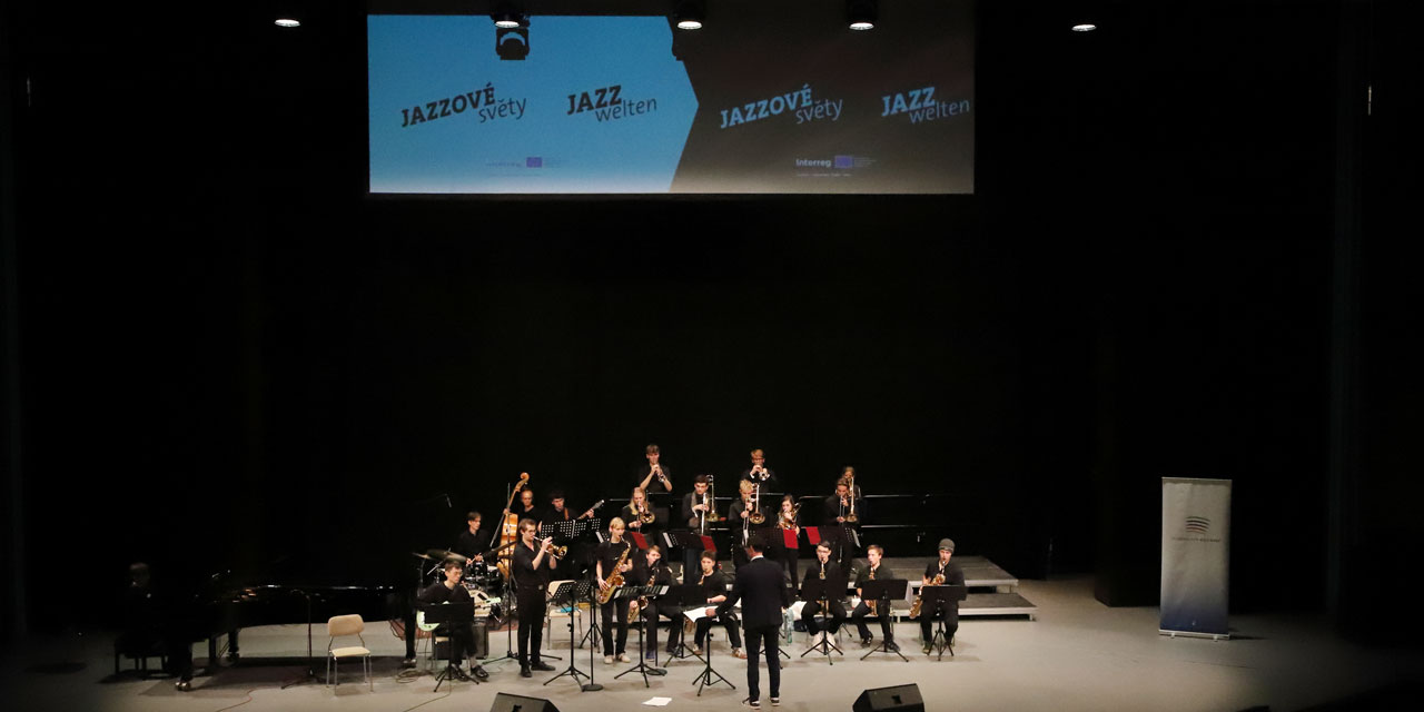 Ein Jazzorchester spielt auf einer Bühne und im Hintergrund ist ein Banner mit der Aufschrift JAZZwelten.
