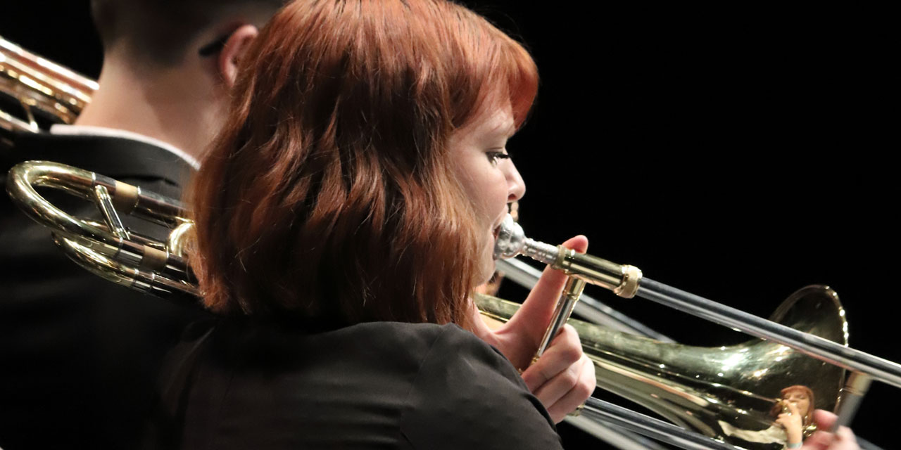 Ein Posaunenspieler und eine Posaunenspielerin mit roten schulterlangen Haaren spielen konzentriert ihr Instrument.