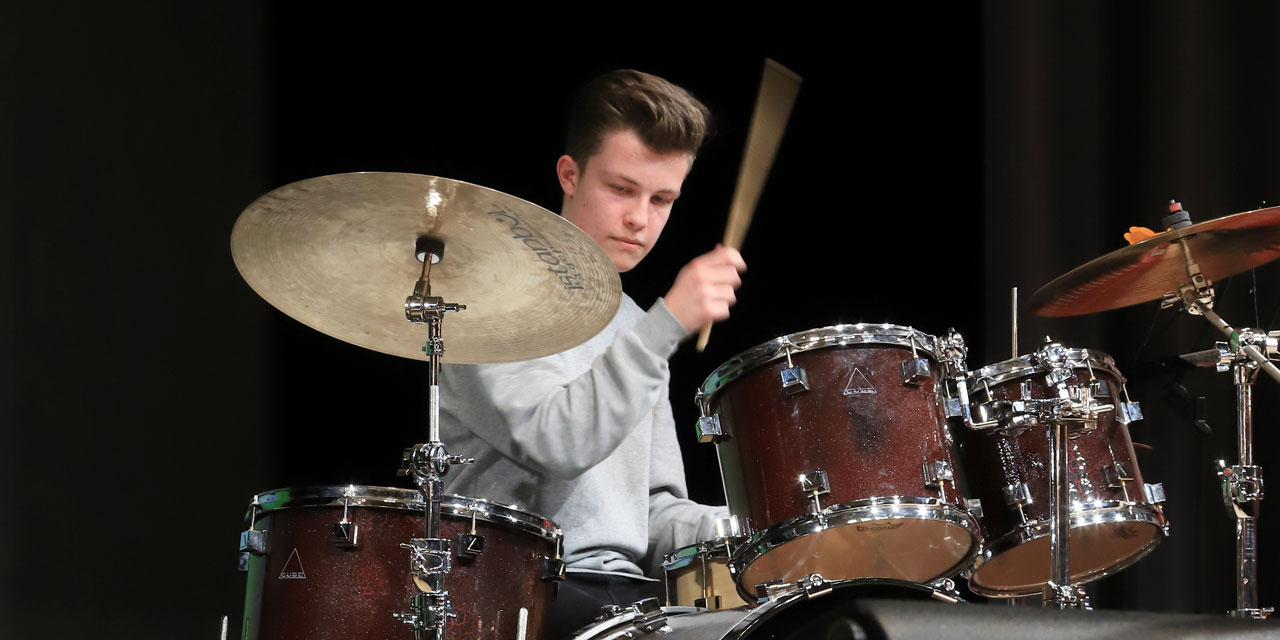 Ein Jugendlicher holt aus zum Schlag auf eine Trommel seines Drumsets.