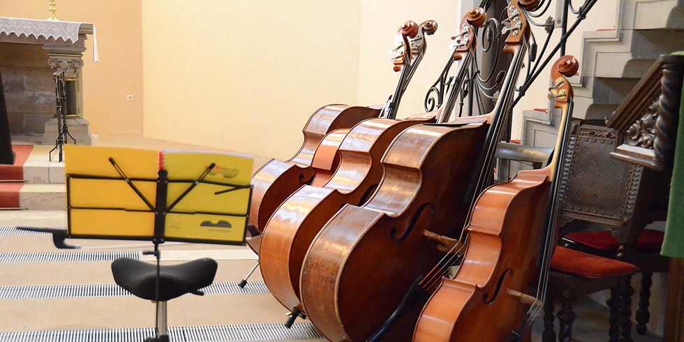 Drei Kontrabässe und zwei Celli lehnen an einer Sitzbank vor einer Treppe.