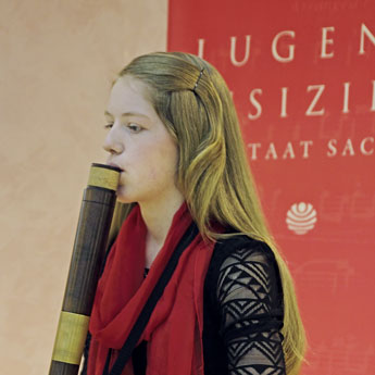 Eine junge Frau mit langen blonden Haaren und rotem Schal spielt vor ein Holzblasinstrument