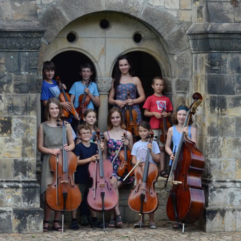 Zehn Kinder mit Streichinstrumenten stehen in einem schloss artigen Eingang  
